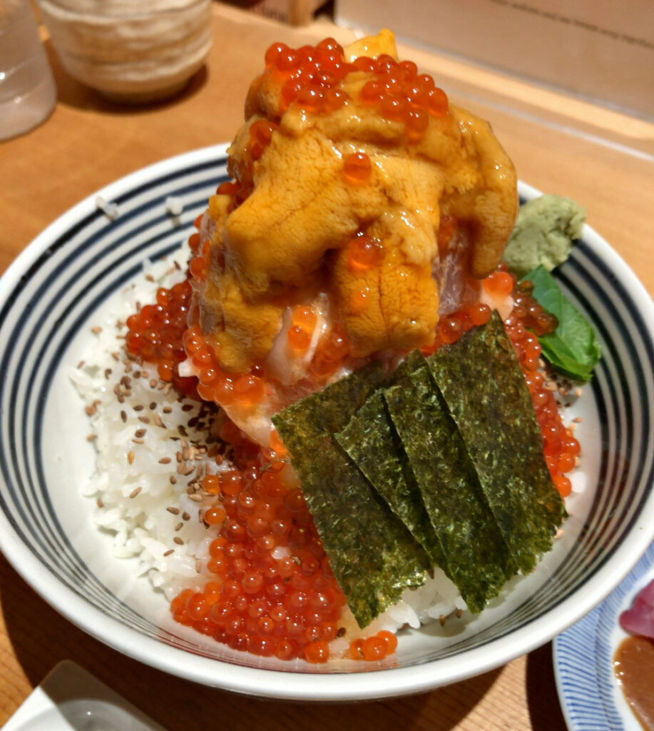 Close-up of the Tokujo Don at Tsujihan Nihonbashi, topped with fresh sea urchin and salmon roe over rice. （つじ半日本橋店の贅沢丼・特上のアップ）